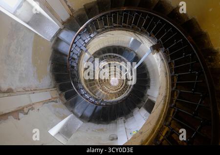 Blick hinunter auf eine alte Wendeltreppe aus Holz und Schmiedeeisen im baufälligen cremeweißen Innenraum des Phare de Calais, einem alten Leuchtturm. Stockfoto