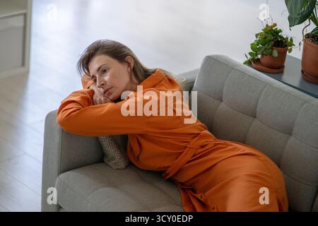 Traurige Frauen mittleren Alters emotionale Schmerzen, die aus gescheiterter Beziehung stammen, die auf der Heimcouch liegt Stockfoto