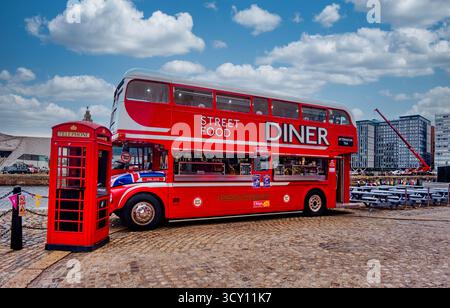 LIVERPOOL, ENGLAND - 18. August 2025: Ein umgerichteter roter Londoner Doppeldeckerbus dient heute als Street Food Diner im Albert Dock, neben einem klassischen Straßencafé Stockfoto
