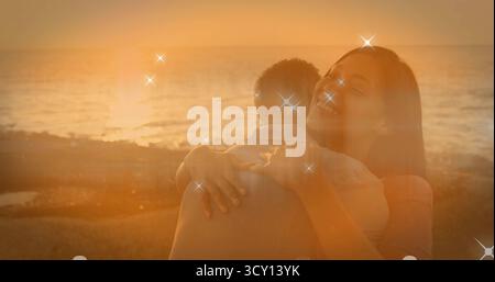 Umarmtes Paar mit lässiger Kleidung an der felsigen Küste bei Sonnenuntergang, mit goldenem Glitzereffekt Stockfoto