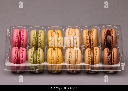Draufsicht auf verschiedene bunte Macarons, verpackt in einer transparenten Kunststoffbox auf grauer Oberfläche. Köstliche französische Süßigkeiten mit minimaler Zusammensetzung. Stockfoto