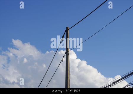 Ein Versorgungsmast mit Stromleitungen gegen einen blauen Himmel und Wolken Stockfoto