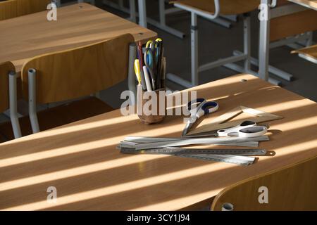 Ein Schulpult mit verschiedenen Schreibwaren, darunter Stifte, Scheren und Lineale, beleuchtet durch Sonnenlicht. Stockfoto
