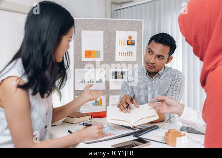 Eine Gruppe multikultureller Kollegen in einem modernen Büro, die Daten und Marketingberichte diskutieren. Das Team konzentriert sich auf die Analyse von Leistungsdiagrammen und pla Stockfoto