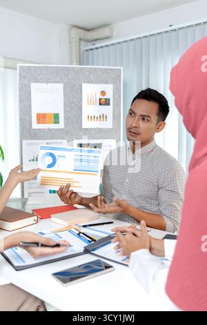 Eine Gruppe multikultureller Kollegen in einem modernen Büro, die Daten und Marketingberichte diskutieren. Das Team konzentriert sich auf die Analyse von Leistungsdiagrammen und pla Stockfoto