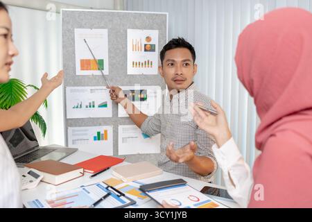 Eine Gruppe multikultureller Kollegen in einem modernen Büro, die Daten und Marketingberichte diskutieren. Das Team konzentriert sich auf die Analyse von Leistungsdiagrammen und pla Stockfoto