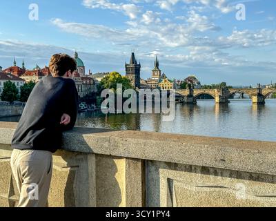Junger Mann blickt bei Abendlicht über die Moldau in Richtung Karlsbrücke und Altstadt-Skyline in Prag, Tschechische Republik Stockfoto