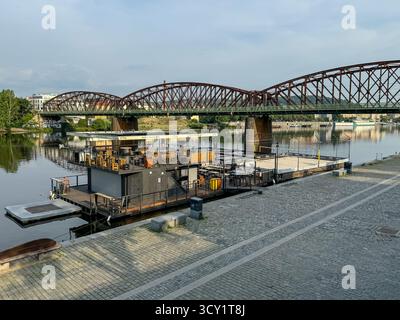 Fußgängerbrücke im industriellen Stil und schwimmende Barplattform an der Moldau in Prag, Tschechische Republik. Stockfoto