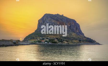 HDR, beeindruckender Felsen am Meer in warmem Sonnenaufgangslicht, ruhige Wasseroberfläche, Monemvasia, Monemvassia, Malvasy, kleine byzantinische Stadt, felsige Insel, Festung Stockfoto