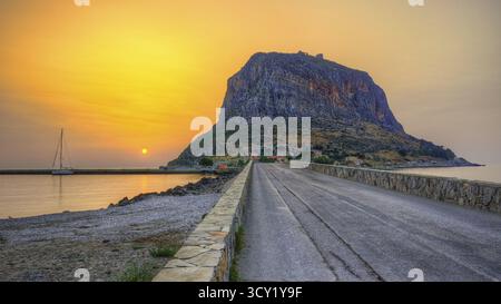 HDR-Straße führt zu einem imposanten Berg am Meer im sanften Licht des Sonnenaufgangs, Monemvasia, Monemvassia, Malvasy, kleine byzantinische Stadt, felsige Insel, Stockfoto