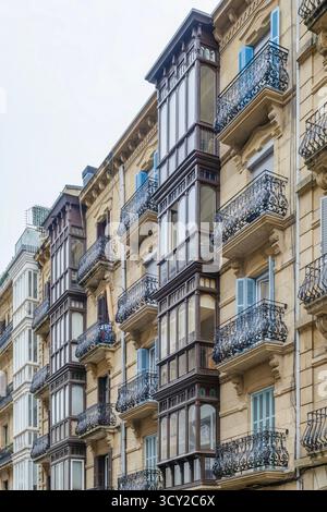 Die kunstvoll verzierte Fassade historischer Wohngebäude in San Sebastian bietet detaillierte schmiedeeiserne Balkone und traditionelle Holzfenster Stockfoto
