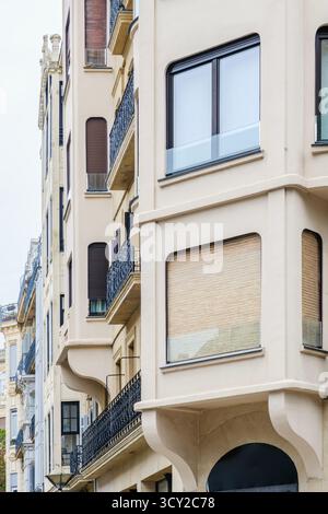 Nahaufnahme einer modernen Stadtfassade mit glatten beigefarbenen Wänden und Fenstern mit abgerundeten Ecken, die einen scharfen Kontrast zum traditionellen Wrap bilden Stockfoto