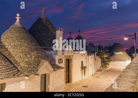 Ein atemberaubender Sonnenaufgang über Alberobello, Apulien, Italien, mit bunten Wolken, die den Himmel über den historischen Trulli-Häusern bemalen. Die sanften Straßenlaternen Stockfoto