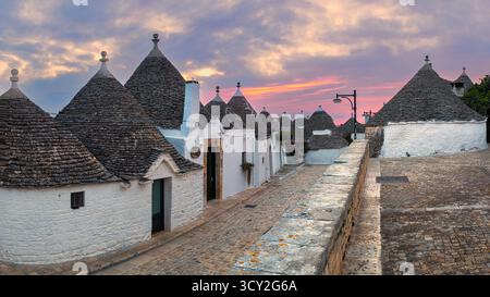 Ein atemberaubender Sonnenaufgang über Alberobello, Apulien, Italien, mit bunten Wolken, die den Himmel über den historischen Trulli-Häusern bemalen. Die sanften Straßenlaternen Stockfoto