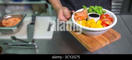 Banner des nicht erkennbaren Küchenchefs, der frische bunte Poke-Schüssel mit Lachs in der Restaurantküche zeigt Stockfoto