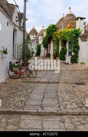 Ein ruhiger Blick am frühen Morgen auf die leeren Straßen von Alberobello, Apulien, Italien. Die traditionellen weißen Trulli-Häuser mit ihren konischen Dächern säumen die Stockfoto