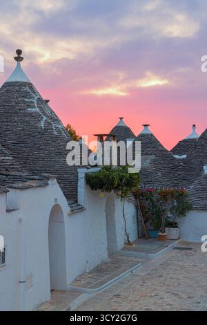 Ein atemberaubender Sonnenaufgang über Alberobello, Apulien, Italien, mit bunten Wolken, die den Himmel über den historischen Trulli-Häusern bemalen. Die sanften Straßenlaternen Stockfoto