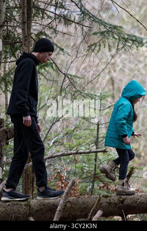 Zwei Kinder durchqueren einen hölzernen Pfad in einem ruhigen Wald, in farbenfrohen Jacken gekleidet, während sie die natürliche Umgebung erkunden, mit Bäumen, die eine Laune erzeugen Stockfoto