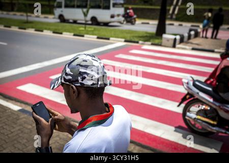 RWA RUANDA RUANDA Kigali Ein Jugendlicher mit Tarnmütze schaut auf sein Handy, während er die Straße entlang läuft Stockfoto