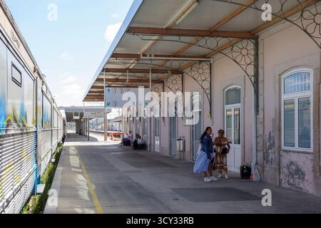 Menschen warten auf einem Bahnsteig an einem Bahnhof mit bogenförmiger Architektur und einem stationären Zug im Hintergrund in Figueira da Foz, Portugal, Europa Stockfoto