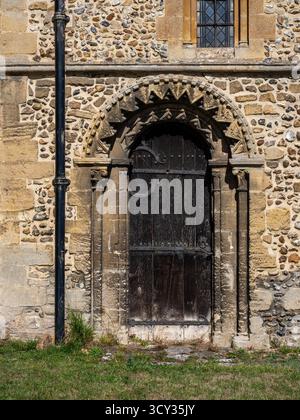 Hölzerne Seitentür mit kunstvoll geschnitzten Steinumrandungen an der Kirche St. Nicholas aus dem 12. Jahrhundert, Castle Hedingham, Essex, Großbritannien Stockfoto