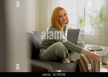 Frau mittleren Alters, die von zu Hause aus arbeitet und eine Tasse Kaffee trinkt Stockfoto