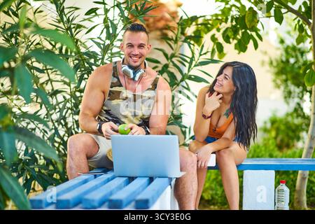 Glücklicher Mann mit Apfel, sitzt auf der Bank mit Laptop und Frau Stockfoto