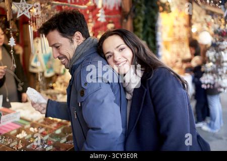 Glückliche Frau, die sich auf den Rücken des Mannes stützt, der auf dem weihnachtsmarkt einkaufen will Stockfoto