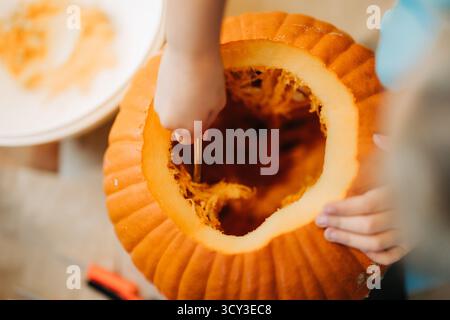 Kind schöpft Kürbisinhalt während halloween-Schnitzerei Stockfoto