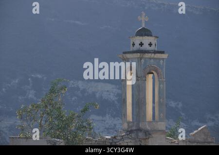 Ein verwitterter Glockenturm erhebt sich aus den Überresten einer alten Kirche, die sich in einer ruhigen Gegend befindet, umgeben von Bergen und Bäumen. Die Szene fängt einen Sen ein Stockfoto