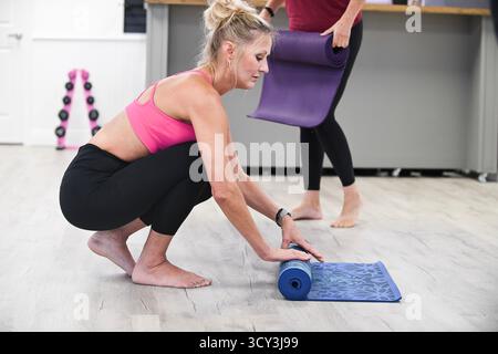 Frau, die nach dem Unterricht hockt und Yoga-Matte aufrollte. Stockfoto