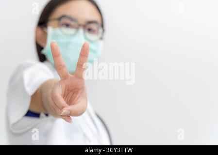 Studio Portrait Asiatische junge Frau Arzt Nahaufnahme Raise zwei V-Form Finger Tragen Sie eine Maske zur Sicherheit Coronavirus im Kampf gegen Krankheit ep zu unterstützen Stockfoto