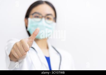 Asiatische junge Frau Arzt tragen Maske zur Sicherheit Coronavirus, Closeup Arzt zeigen Daumen bis zu einem Patienten im Kampf gegen Krankheit Epidemie C zu unterstützen Stockfoto