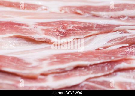Close up top view Pack Speck, Stücke rohes Fleisch von frischem rotem Schweinefleisch mit weißen Fettscheiben werden in dünne Streifen übereinander gestapelt geschnitten Stockfoto