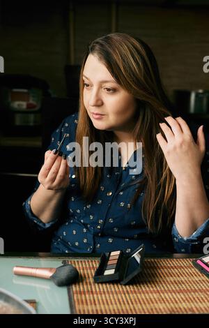 Frau, die Make-up aufträgt, während sie im Spiegel schaut Stockfoto