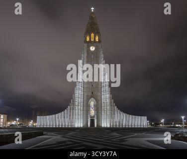 Blick auf die Kirche von Hallgrímskirkja, die vor einem stimmungsvollen Himmel beleuchtet ist, deren hoch aufragender Turm ein Leuchtfeuer in der Nacht, Reykjavik, Island. Stockfoto