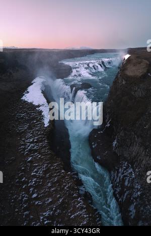 Blick aus der Vogelperspektive auf den majestätischen Gullfoss-Wasserfall, der kraftvoll durch den zerklüfteten Canyon stürzt, dessen eiskaltes Wasser im Kontrast zum dunklen, felsigen Gelände in Reykjavík, Island, steht. Stockfoto