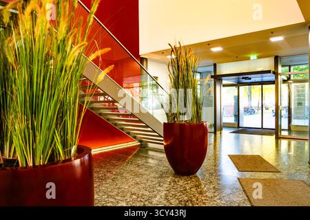 Moderne Bürolobby Mit Großen Pflanzgefäßen Und Glaseingang: Zeitgenössisches Innendesign Mit Warmen Farben, Natürlichem Licht Und Eleganter Architektur Stockfoto