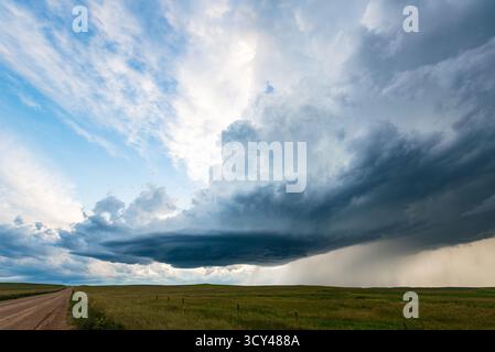 Sturmwolken und Sonnenstrahlen durchbrechen eine staubige Straße und vermischen dramatischen Kontrast, stimmungsvollen Himmel, goldenes Licht, ländliche Landschaft, und die Kraft der Natur Stockfoto