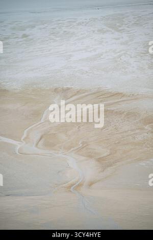 Ein Blick aus der Vogelperspektive fängt die komplizierten Muster von Gezeitenkanälen und Sandbänken in der riesigen Bucht von Mont Saint-Michel in Frankreich an einem klaren Tag ein. Stockfoto