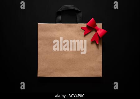 Black Friday Concept mit einer braunen Papiertüte mit roter Schleife und schwarzen Griffen auf dunklem Hintergrund. Stockfoto