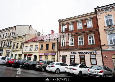 Tarnow, Polen - 10. Oktober 2025: Bunte Schaufensterfronten säumen eine Straße in Tarnow, Polen, mit geparkten Autos und einem Backsteingebäude. Dom Finansowy Stockfoto