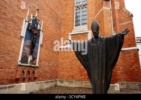 Tarnow, Polen - 10. Oktober 2025: Die Bronzestatue Johannes Paul II. Mit weit offenen Armen steht neben einer roten Backsteinkirche in Tarnow. Stockfoto