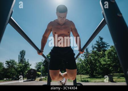 Mann, der Calisthenics-Übungen an Bars im Freien in sonnigem Park macht Stockfoto