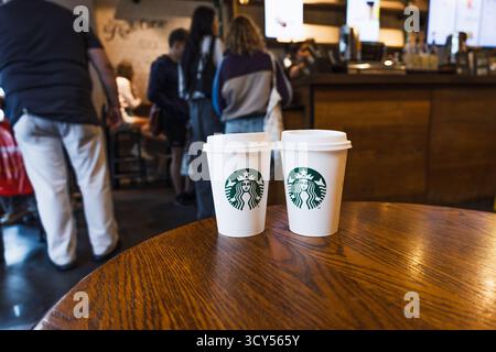Starbucks Kaffeetassen auf Holztisch im belebten Café. London, UK, 8. Juli 2023 Stockfoto