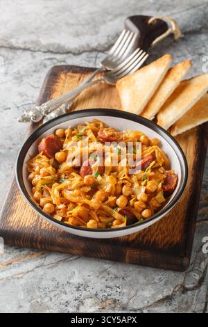 Scharfer Eintopf mit Kichererbsen, Kohl, Paprika, Zwiebeln und Chorizo aus nächster Nähe auf einem Teller auf dem Tisch. Vertikal Stockfoto