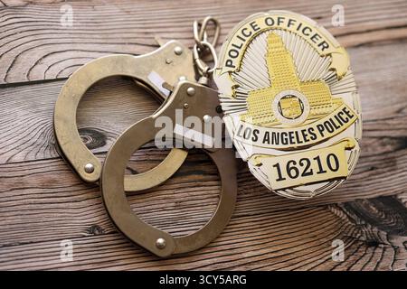 KIEW, UKRAINE - 17. SEPTEMBER 2025 Polizeiabzeichen der US LAPD mit Handschellen auf Holztisch in Nahaufnahme Stockfoto