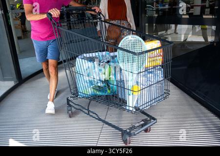 Person, die einen mit Wasserflaschen und anderen Artikeln gefüllten Einkaufswagen beim Verlassen des Supermarktes La Trinite sur Mer in Morbihan in der Bretagne schiebt Stockfoto