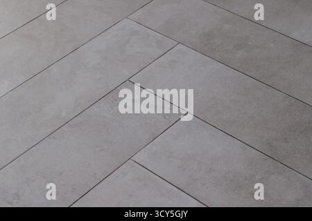 Graue rechteckige Fliesenstruktur im Fischgrätenmuster, das Naturstein imitiert. Stockfoto