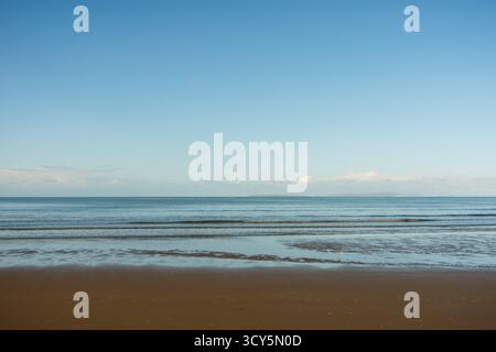 Harlech, Wales – 2025.09.21 – Ein ruhiger Blick auf sanfte Wellen, die auf den Harlech Beach mit sanften Reflexen auf nassem Sand unter einem klaren Morgenhimmel Rollen Stockfoto